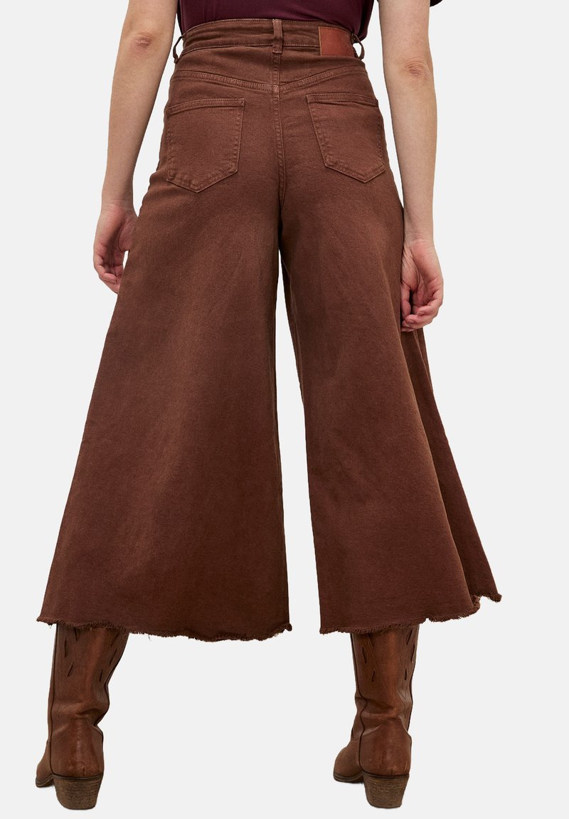 Braune, weit geschnittene Culottes aus Denim mit einem rohen Saum, zwei Gesäßtaschen und einem hohen Bund. Getragen mit braunen Stiefeln.