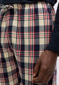 Rutiga pyjamasbyxor i marinblått, krämvitt och rött. Mjuk bomull, elastisk midja med dragsko. Har stort rutmönster och sidofickor.