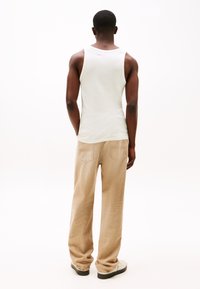 Débardeur en coton blanc associé à un pantalon large beige. Le tissu a une texture douce, et le pantalon possède des poches arrière et une coupe décontractée.