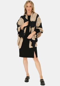 Wzorzysta chusta w kolorze beżowym i czarnym, z motywem róż. Lekki materiał z opadającą sylwetką. Noszona na czarnej sukience.