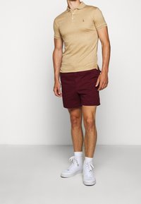 Béžová polos tričko s krátkými rukávy, zdobené malým logem. Vybavené burgundskými šortkami a bílými vysokými teniskami. Jednoduchý design.