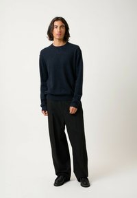 Pull en tricot bleu marine à manches longues, avec des poignets côtelés et un col rond, associé à un pantalon noir ample et des chaussures noires. Design simple.