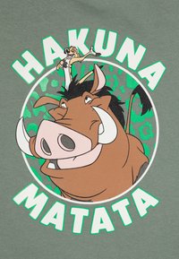Zeleni materijal sadrži crtež u stilu crtanog filma s nasmijanim veprom i malim likom iznad, okruženim kružnim uzorkom i natpisom "HAKUNA MATATA".