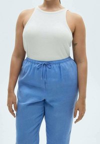 Bílý bezrukávový top s kulatým výstřihem, kombinovaný se světle modrými volnými kalhotami s páskem na stažení z měkké tkaniny.