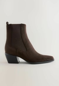 Bottine en daim brun avec des panneaux élastiques sur les côtés, bout pointu et un petit talon carré incliné. Elle dispose d'une languette à l'arrière.