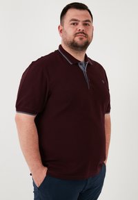 Burgundské polo tričko se šedým límcem, krátkými rukávy se šedým akcentem, dvou knoflíkovým zapínáním a malým logem na hrudi.