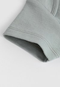 Cuff in cotone grigio, con una texture liscia e cuciture pulite. Il polsino è leggermente arrotolato, rivelando una morbida fodera interna.