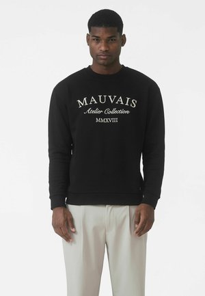 Czarna bluza z okrągłym dekoltem, z białym napisem: "MAUVAIS Atelier Collection MMXVIII." Materiał wygląda na miękki, z prążkowanymi mankietami.