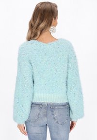 Türkiser, flauschiger Pullover mit lockerer Passform, geripptem Saum und Glockenärmeln. Er weist mehrfarbige Sprenkel im gesamten Stoff auf.