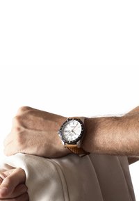 Silver och svart armbandsur med en vit urtavla, brunt läderarmband med perforeringar, som visar datum och veckodag.