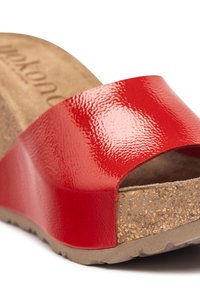 Red patent leather slide sandal with a cork footbed and textured sole. Features a wide, glossy strap and a slight wedge heel.