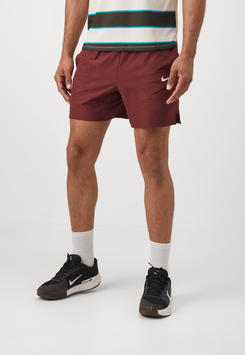 Muške bordo atletske kratke hlače sa bočnim džepovima, sa belim Nike logotipom. U kombinaciji sa crno-belim patikama i belim čarapama do gležnja.