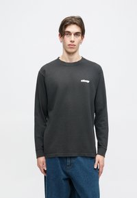 T-shirt de algodão cinza escuro de mangas longas com um logótipo branco no lado esquerdo do peito, decote redondo e ajuste descontraído.