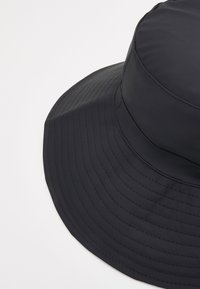 Black bucket hat made of smooth fabric, featuring a wide, stiff brim and a structured top, with visible stitch lines along the edge.