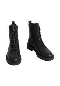 Botas negras de cuero hasta el tobillo con cordones en la parte delantera, cierre con cremallera lateral, suela gruesa y lengüeta en la parte trasera para facilitar su uso.