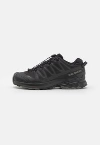 Black trail running shoes with a textured surface, mesh details, quick-lace system, and a rugged rubber sole for enhanced grip and support.