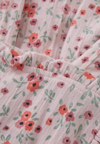 Pink stof med en struktureret, ribbet mønster, prydet med et blomstermønster af røde, lyserøde og grønne blomster. Blødt, sammenkrøllet detaljering tilføjer dimension.