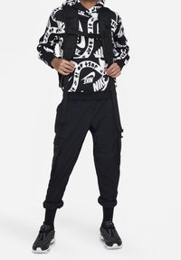 Mustalla ja valkoisella hupparilla, jossa on rohkeat "Nike"-grafiikat, mustat cargo-housut ja mustat kengät, joissa on valkoisia yksityiskohtia. Reppu mustilla hihnoilla.