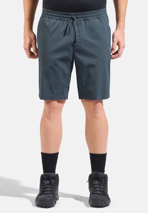 Herren-Shorts in Dunkelgrau, aus leichtem Stoff, mit elastischem Bund und Kordelzug, knielang, kombiniert mit dunklen Socken und Wanderschuhen.