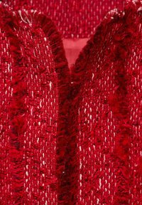 Rot strukturierter Stoff mit einem gewebten Muster. Ausfransende Kanten verleihen eine taktile Qualität, die die visuelle Tiefe und den Reichtum des Materials verstärkt.