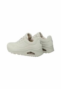 Zapatos deportivos de color beige claro con parte superior texturizada, cierre de cordones y amortiguación de aire visible en la suela. Acabado suave y minimalismo en el branding.