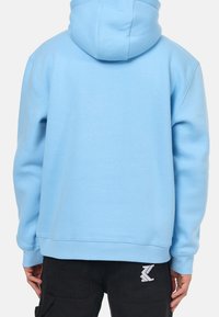 Sudadera azul claro con un bolsillo canguro, puños y dobladillo acanalados. Cuenta con una capucha ajustable con cordón y un pequeño logo en la cinturilla.