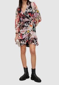 Robe portefeuille florale avec des imprimés vibrants en rouge, rose et noir, dotée de longues manches bouffantes et d'un ourlet volanté. Associée à des bottines noires.