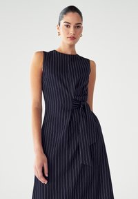 Marineblauw gestreepte jurk met een mouwloos ontwerp, voorzien van een gedraaide knoopdetail op de taille en een A-lijn silhouet. Gladde textuur.