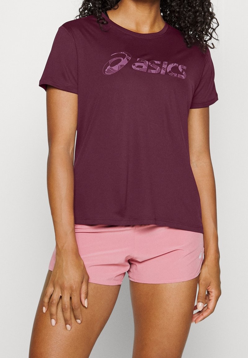 Camiseta deportiva burdeos de manga corta con logo Asics tonal, combinada con pantalones cortos rosas, con un ajuste relajado y textura suave.