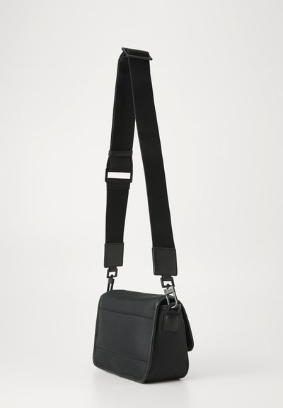 Sac à bandoulière noir en tissu texturé, de forme rectangulaire, avec une bandoulière réglable et un fermoir magnétique.