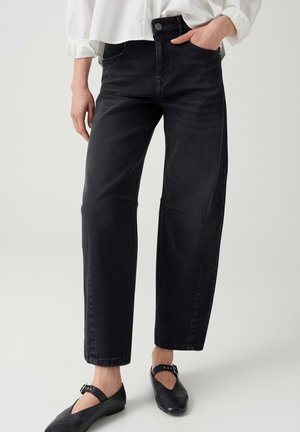Person trägt schwarze High-Waist-Jeans mit geraden Beinen, kombiniert mit schwarzen Schnallenschuhen und einem weißen Langarmhemd.