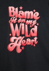 Schwarzes T-Shirt mit fettem pinkem Text: "Gib meinem WILDEN Herzen die Schuld" und Sternakzenten. Glatte Stoffqualität, lässiges Design, kontrastierende Farben.