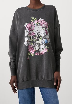 Grå oversized sweatshirt med et blomsterkraniumprint. Har ribstrikkede manchetter og kant. Designet inkluderer farverige blomster og tekst. Blødt materiale.
