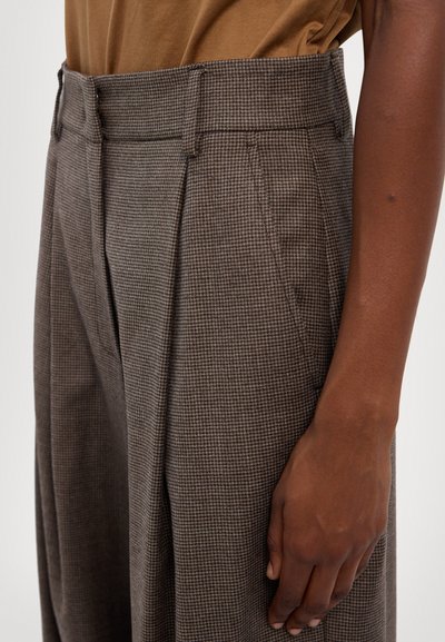 Pantalones de cuadros marrones con pliegues, que presentan un corte ajustado, presillas para el cinturón y una textura suave. Se aprecia el detalle de los bolsillos laterales.