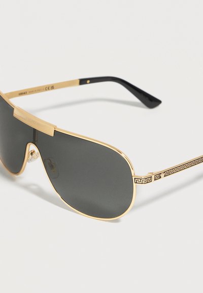 Γυαλιά ηλίου aviator με χρυσό πλαίσιο, σκουρόχρωμους φακούς, μαύρες άκρες στα μπράτσα και διακοσμητικό ελληνορωμαϊκό μοτίβο στα πλαΐνά μέρη.