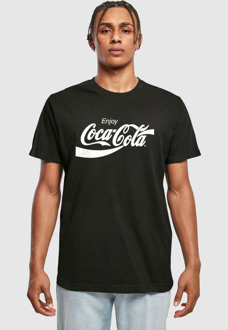 Černé bavlněné tričko s nápisem "Enjoy Coca-Cola" v bílém kurzívním písmu přes hruď, s klasickým kulatým výstřihem.