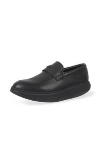Zapato negro de cuero sin cordones con textura suave, diseño de punta redondeada y una ligera suela con plataforma. Presenta un acento de correa en la parte delantera.