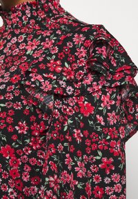 Svart tyg med små röda och rosa blommönster. Volangdetalj på axeln tillför textur till designen.