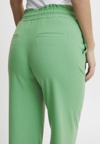 Green, stretchy pants with a smooth texture, featuring a relaxed fit, elastic waistband, and two back pockets.