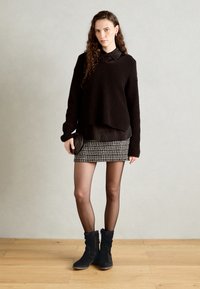 Czarny, oversize sweter dzianinowy, nałożony na czarną koszulę z guzikami. Krótka spódnica w wzór houndstooth, przezroczyste rajstopy i czarne zamszowe botki za kostkę.