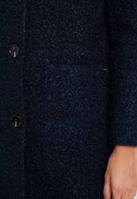 Cappotto in lana texturizzata di colore navy con chiusura a bottone, tasca a toppa e morbido motivo in rilievo.