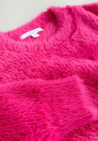 Chlpatý ružový sveter s okrúhlym výstrihom a mäkkou textúrou. Na štítku je nápis "NEXT." Detailný záber ukazuje živé farby a nadýchaný materiál.