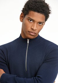 Sininen korkeakauluksinen villapaita, jossa on puolivetoketju, valmistettu pehmeästä, tekstuurista kankaasta. Ominaisuuksiin kuuluvat pitkät hihat ja istuva siluetti.