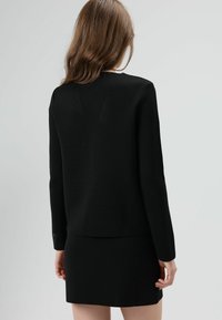 Zwarte top met lange mouwen van gestructureerde stof, rechte zoom en lichte schoudervulling, gecombineerd met een zwarte minirok. Eenvoudig en modern ontwerp.