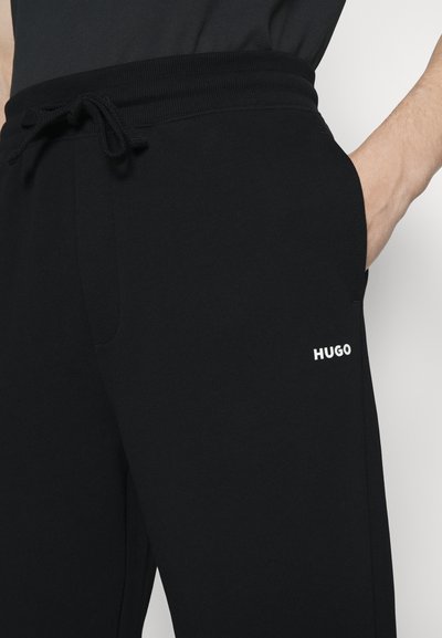 Pantalons de jogging noirs avec une taille à cordon, poches latérales et logo "HUGO" blanc sur la cuisse, fabriqués en tissu doux et léger.