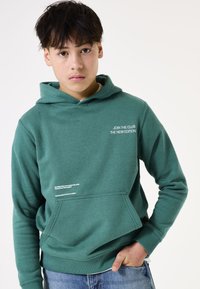 Felpa verde con cappuccio e tasca frontale. Presenta grafiche testuali bianche sul petto e nella parte inferiore frontale. Realizzata in materiale morbido e texture.