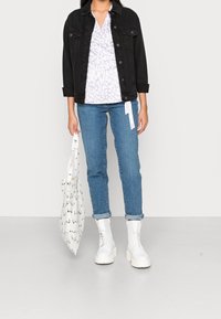 Giubbotto di jeans nero, top avvolgente in stampa leopardata lavanda, jeans blu, stivaletti bianchi con lacci spessi e una borsa tote bianca con disegni neri.