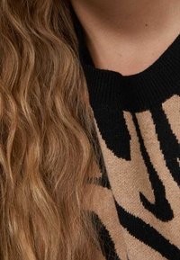 Czarny i beżowy sweter w wzór zebry, z prążkowanym czarnym dekoltem. Miękka tekstura z widocznymi detalami szwu.