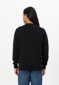 Black sweatshirt with ribbed cuffs and hem, featuring a crew neck and a smooth texture. Paired with blue denim jeans.