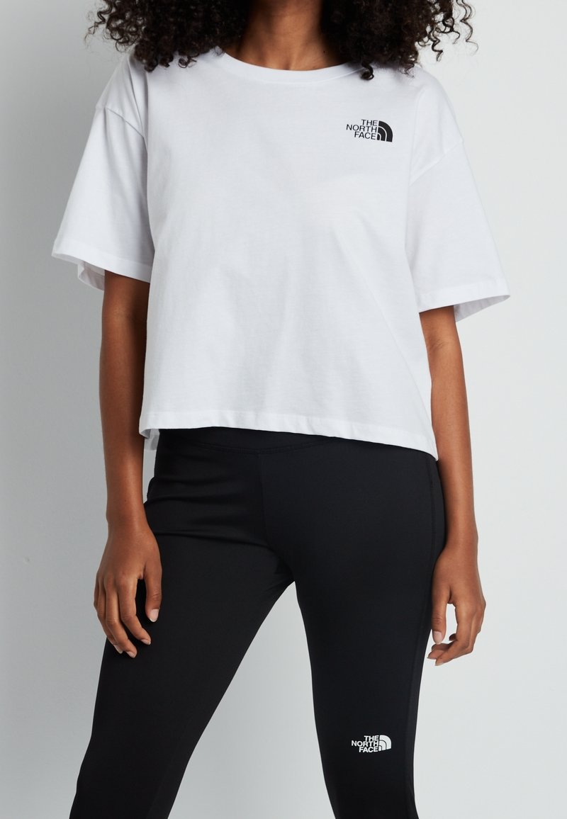 Witte cropped t-shirt met korte mouwen en een zwart logo op de borst, gecombineerd met zwarte legging met een wit logo op het been.